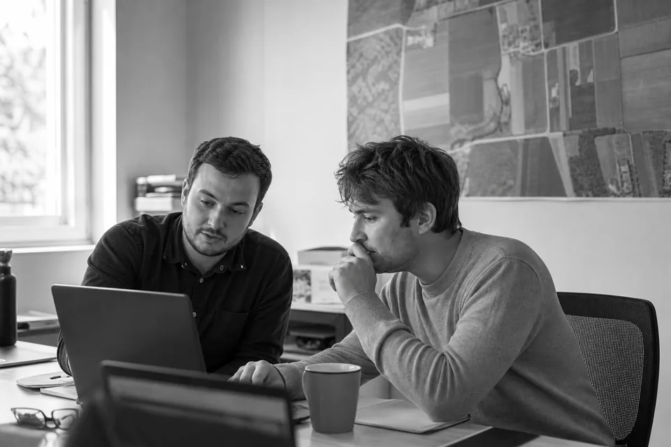 Two developers at a table reviewing parcel data on a laptop in a small office